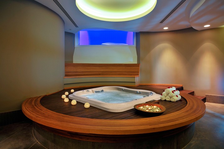 an indoor hot tub on a circular platform with candles and flowers